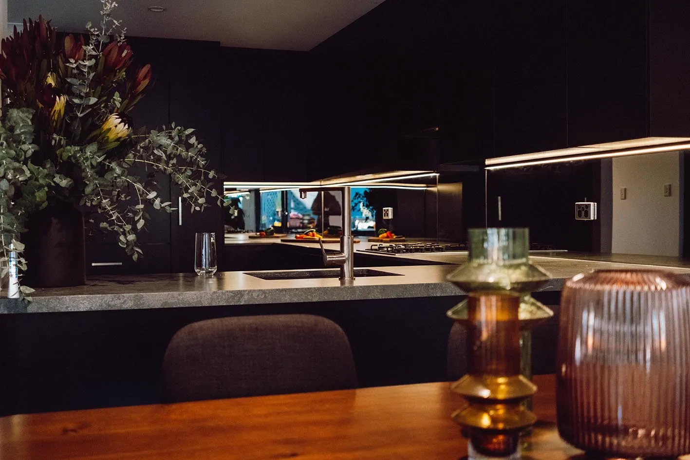 A dark-toned kitchen with native flowers and warm under-cabinet lighting