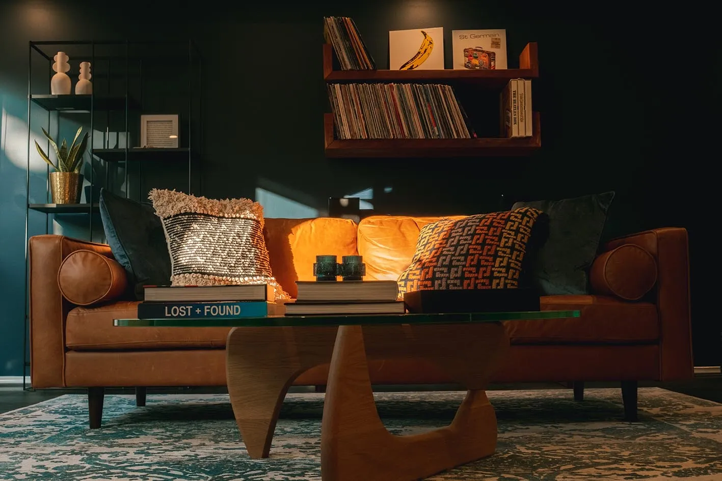 A tan leather sofa beneath shelves of vinyl records in a moody lounge designed by Markus Hamence