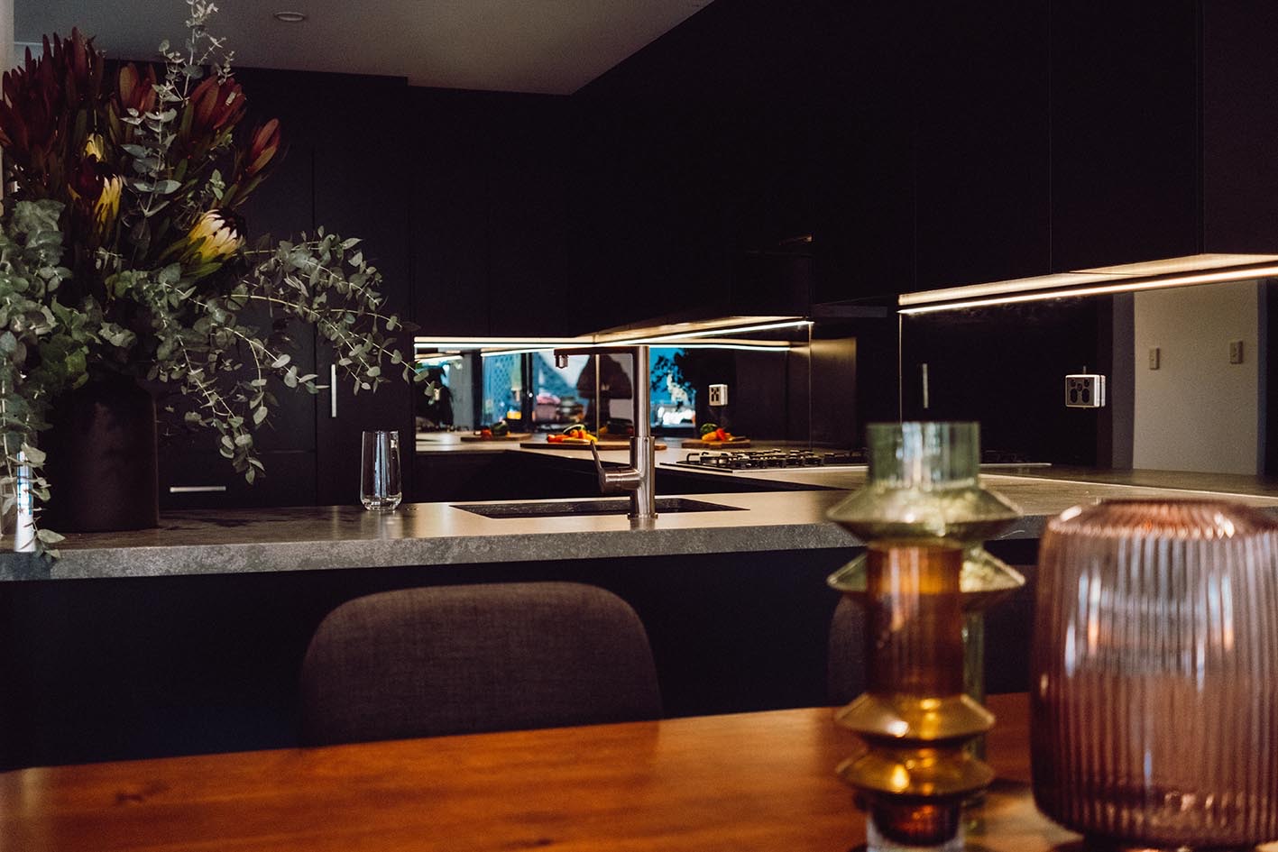 A dark-toned kitchen with native flowers and warm under-cabinet lighting