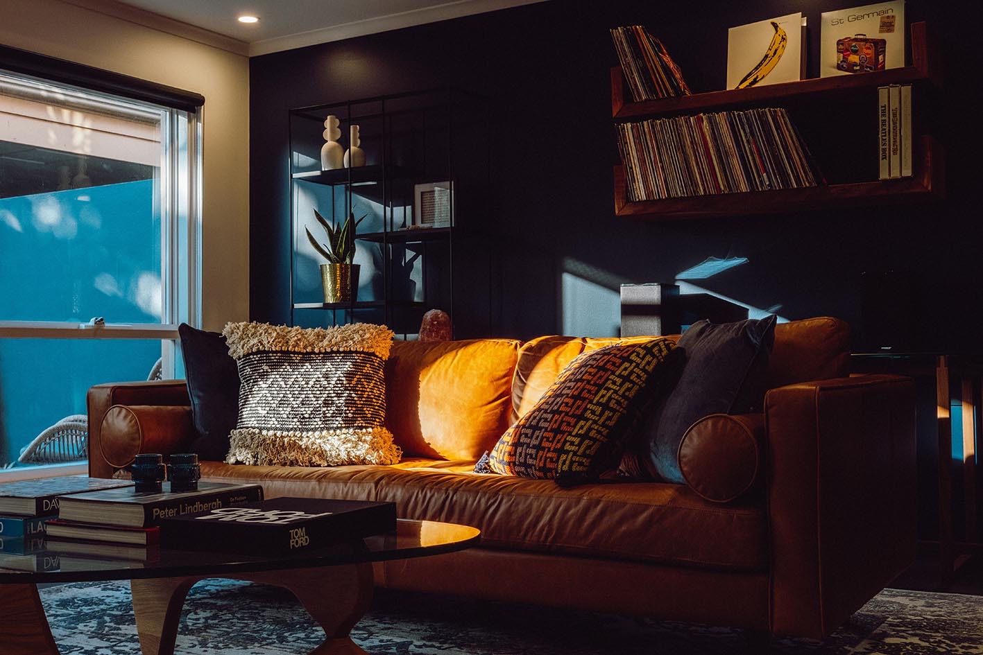 Afternoon light falling across a tan leather sofa in a dark-toned living room