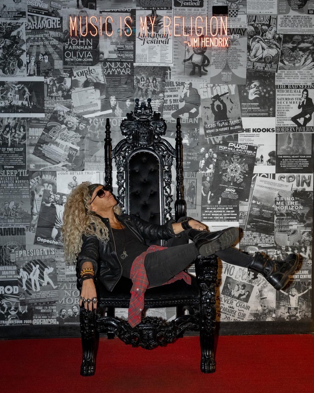 Markus Hamence lounging on a black throne against a wall of gig posters